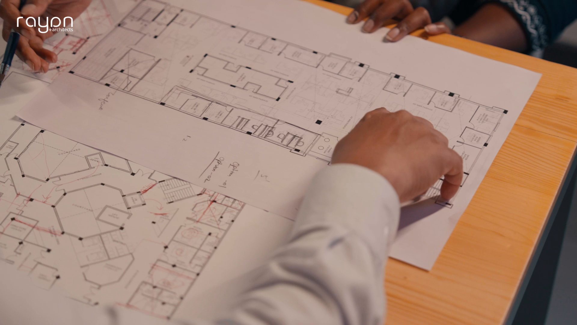 Still from the Rayan Architects studio film: hands marking up a floor plan
